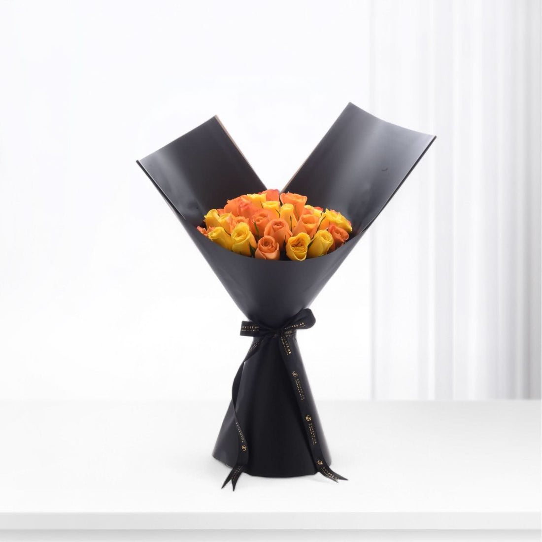 Vibrant orange-yellow roses elegantly wrapped in matte black paper with gold-trimmed ribbon.