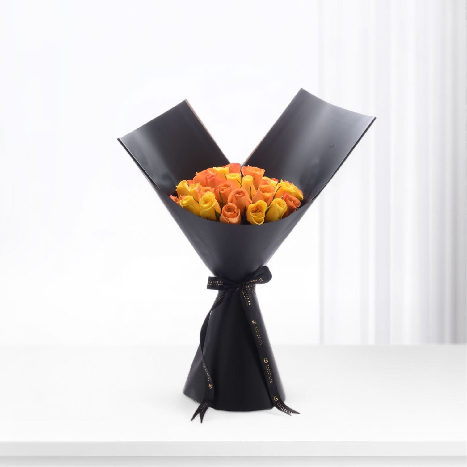Vibrant orange-yellow roses elegantly wrapped in matte black paper with gold-trimmed ribbon.