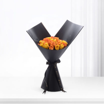 Vibrant orange-yellow roses elegantly wrapped in matte black paper with gold-trimmed ribbon.