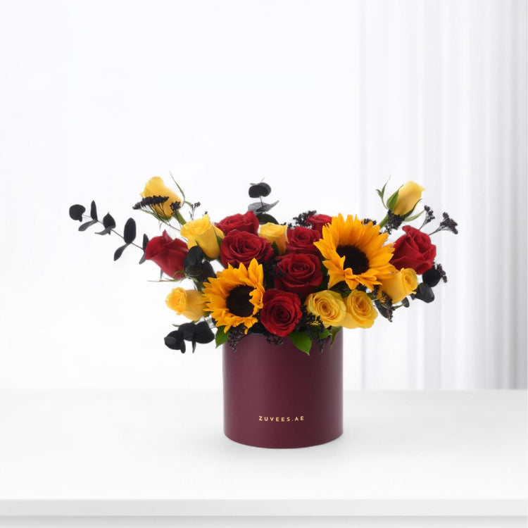 Vibrant red and yellow roses with sunflowers in burgundy cylinder vase.