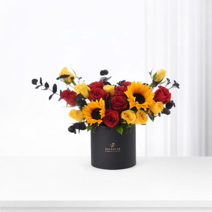 Vibrant red roses and sunflowers in sleek black vase with gold branding.