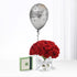 Silver "Happy Birthday" balloon floats above vibrant red roses in glass vase, beside green gift box.
