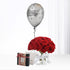Silver "Happy Birthday" balloon floats above vibrant red roses in clear vase with gift box.