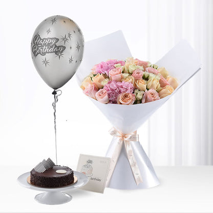 Pastel rose bouquet, silver "Happy Birthday" balloon, chocolate cake, and greeting card on white surface.