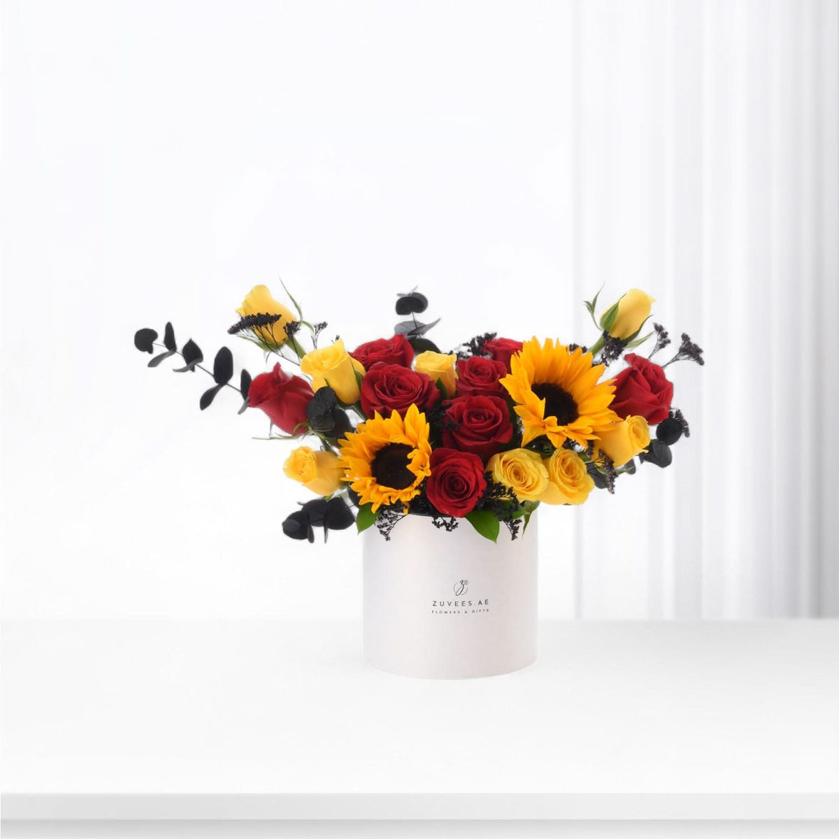 Vibrant red and yellow roses with sunflowers in minimalist white box.