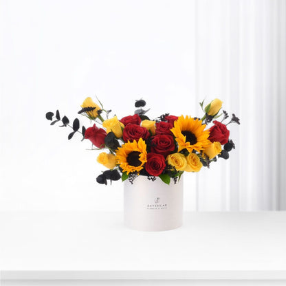 Vibrant red and yellow roses with sunflowers in minimalist white box.