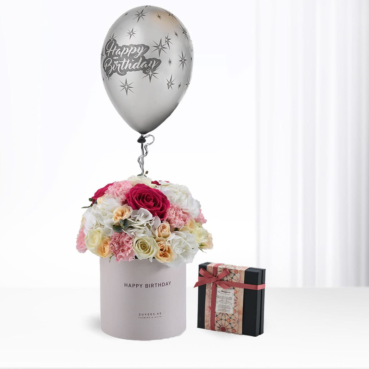 Silver balloon atop floral bouquet in gray box, beside patterned gift.