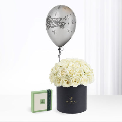 Silver "Happy Birthday" balloon floats above creamy white roses in black cylinder box.