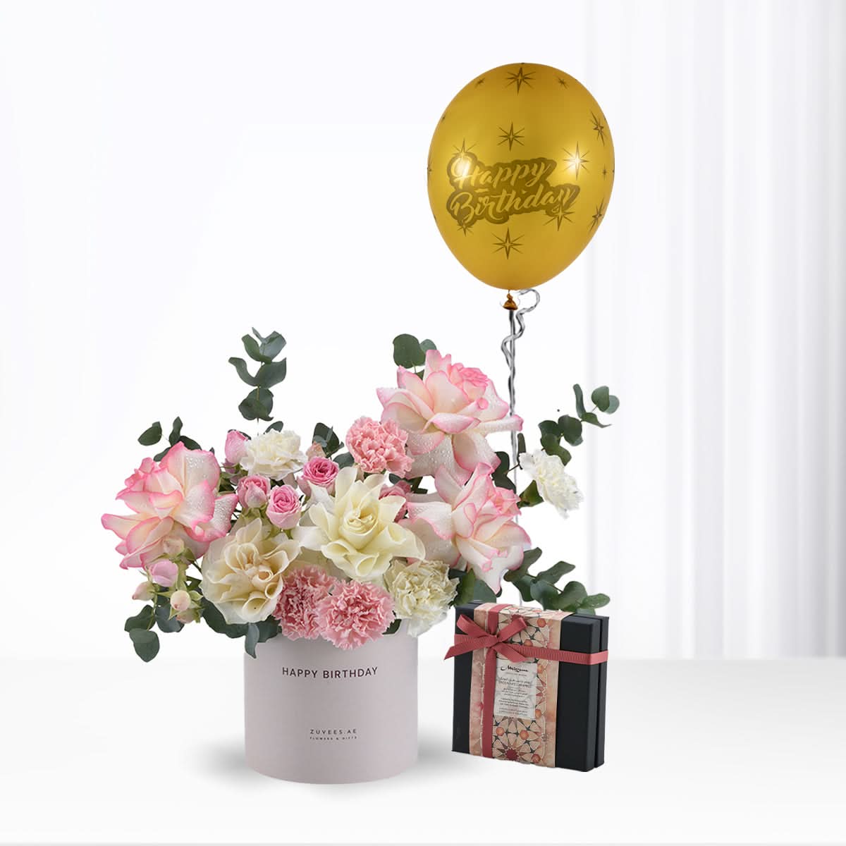 Pink and cream roses, eucalyptus, and a gold "Happy Birthday" balloon with gift box.