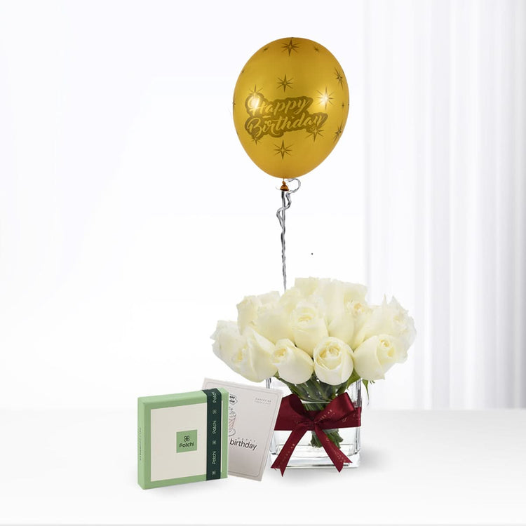 Golden "Happy Birthday" balloon floats above white roses in glass vase with red bow.
