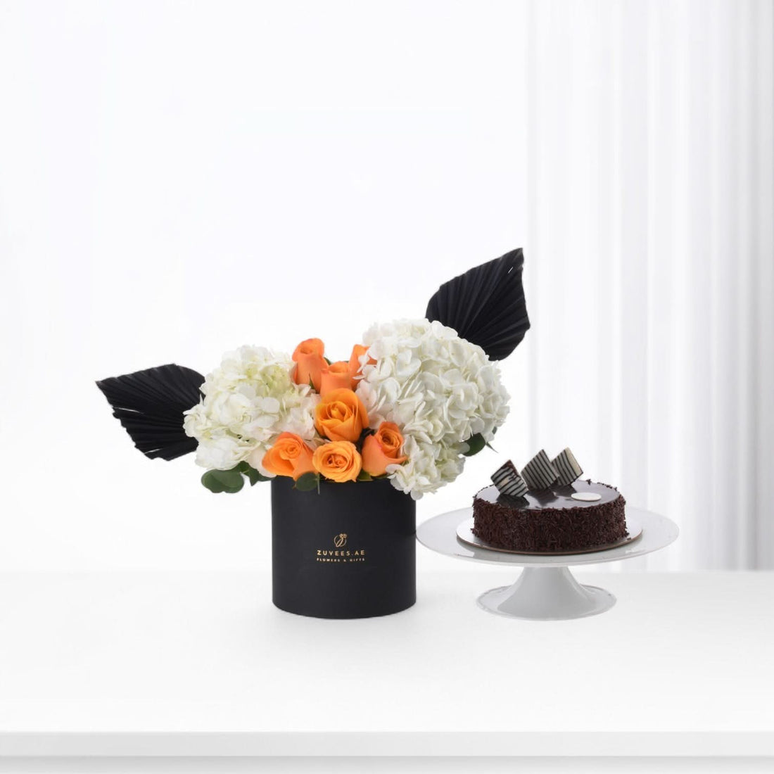 Elegant black box with orange roses, white hydrangeas, and chocolate cake beside it.
