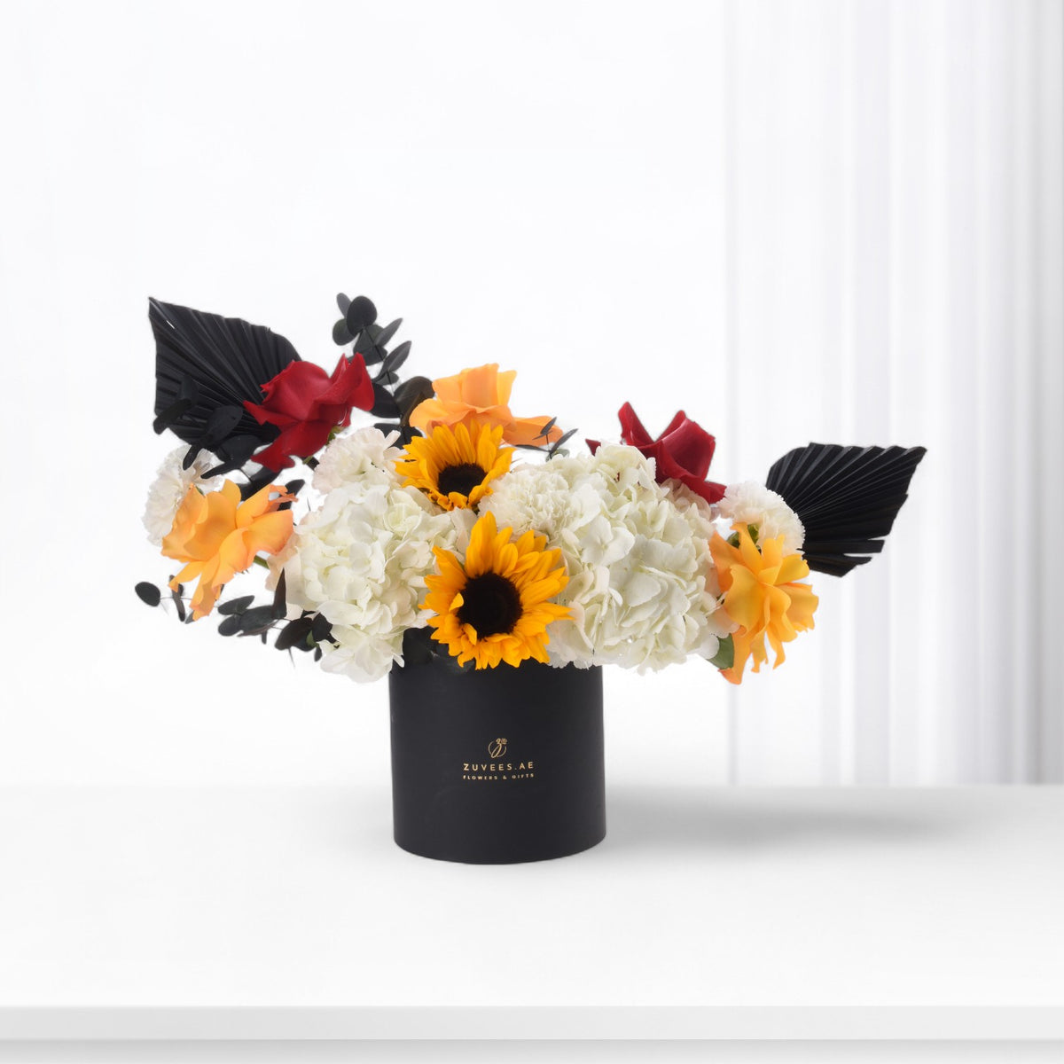 Bold sunflowers, white hydrangeas, and red roses in sleek black vase.