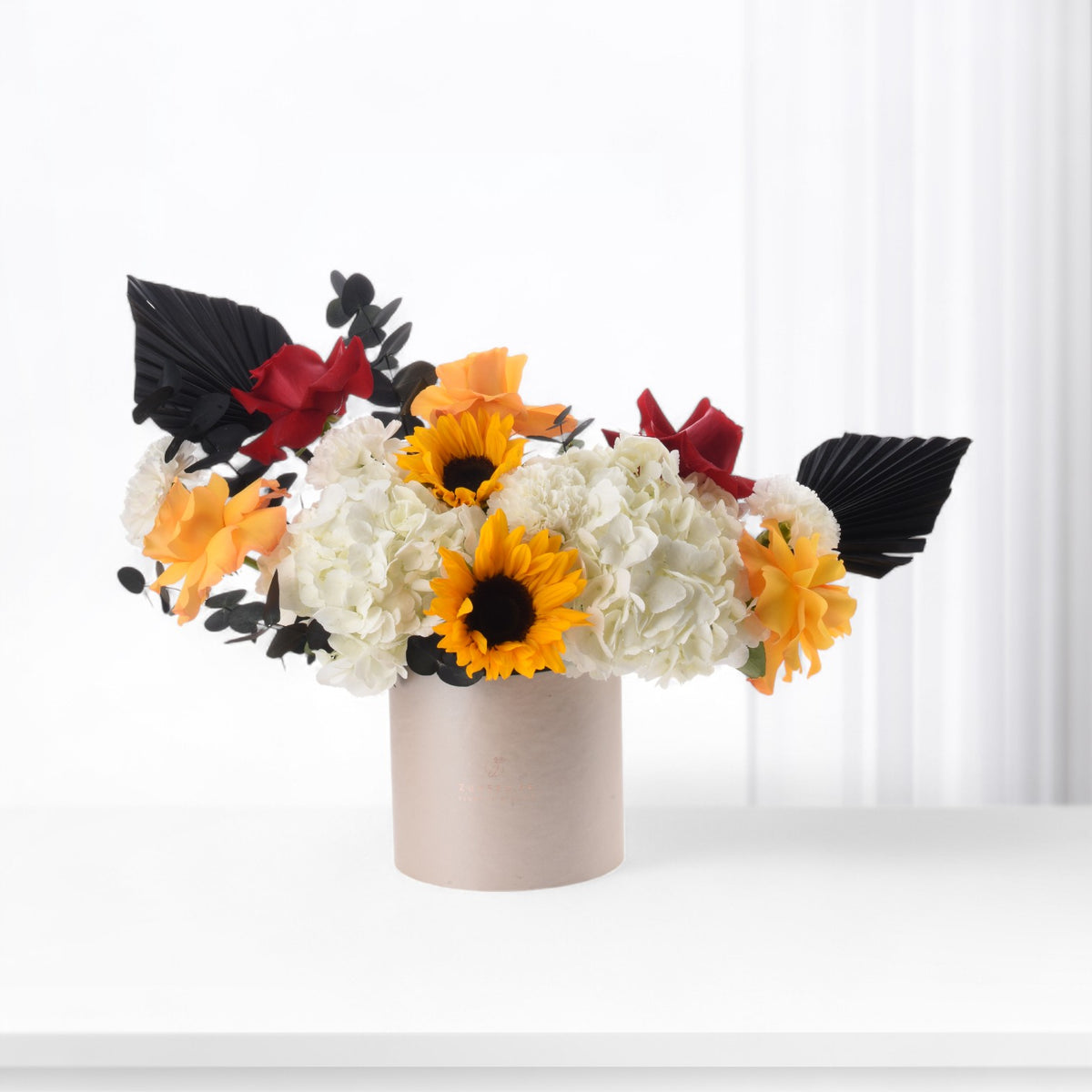 Vibrant sunflowers, white hydrangeas, and red roses in beige vase against bright white background.