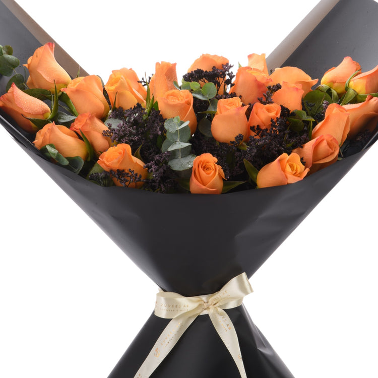 Vibrant orange roses in sleek black wrap, accented with dark foliage and gold ribbon.