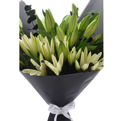 Elegant green-and-white lily bouquet wrapped in matte black paper with white bow.