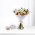 Soft peach roses and orange dahlias wrapped in white paper with branded ribbon, beside elegant gift box and candle.