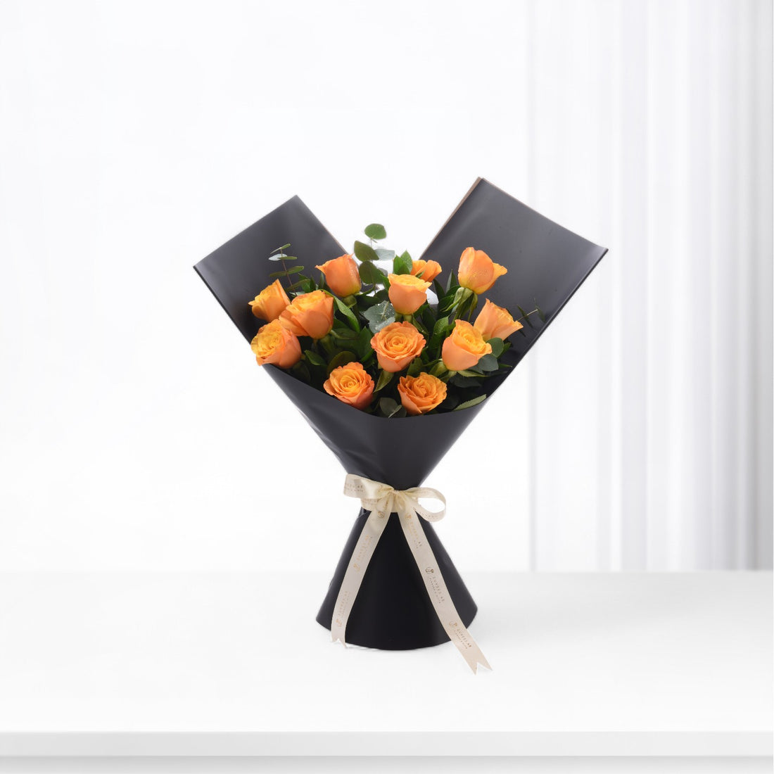 Vibrant orange roses elegantly wrapped in matte black paper with cream ribbon bow.