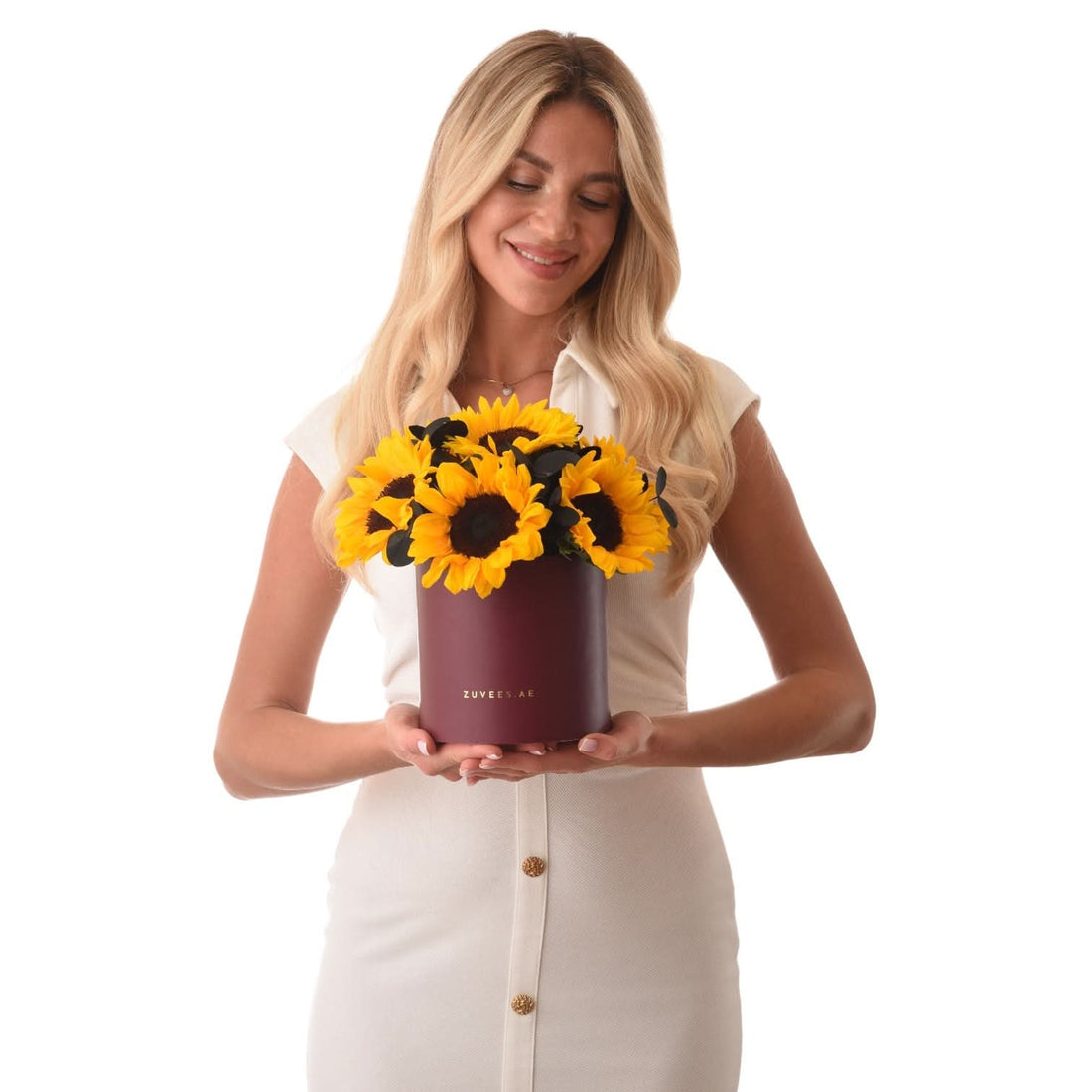 Woman holds burgundy box of vibrant yellow sunflowers with dark centers.