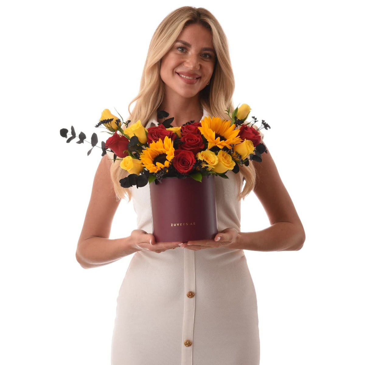 Woman holds burgundy box with vibrant red and yellow roses and sunflowers.
