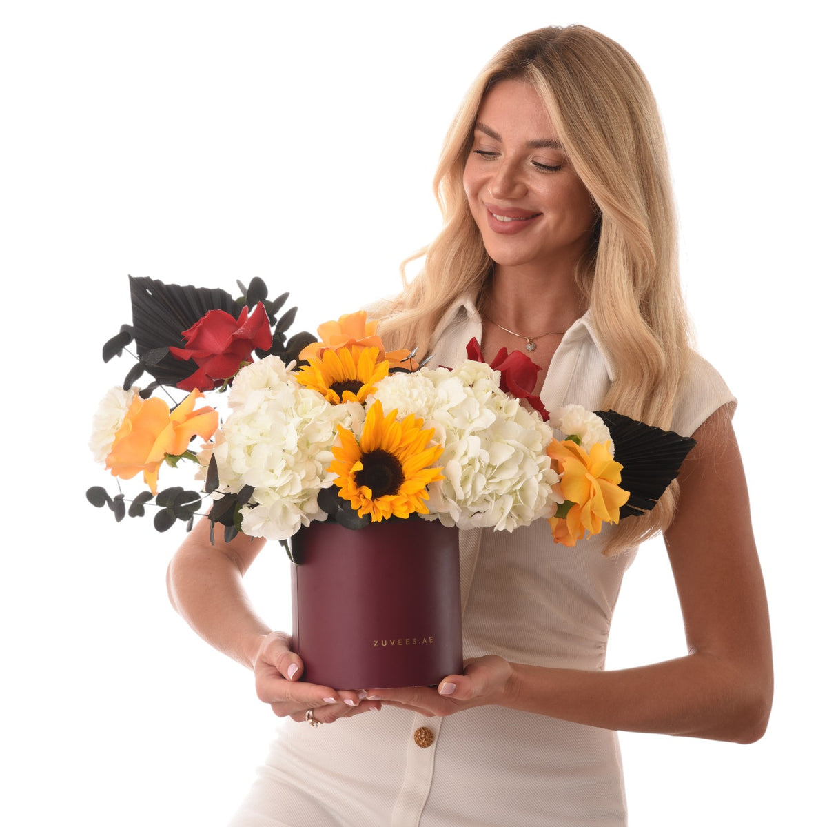 Vibrant sunflowers, white hydrangeas, red roses in burgundy Zuvees box, held by smiling blonde woman.