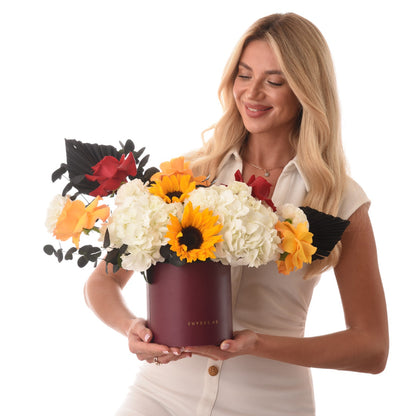Vibrant sunflowers, white hydrangeas, red roses in burgundy Zuvees box, held by smiling blonde woman.