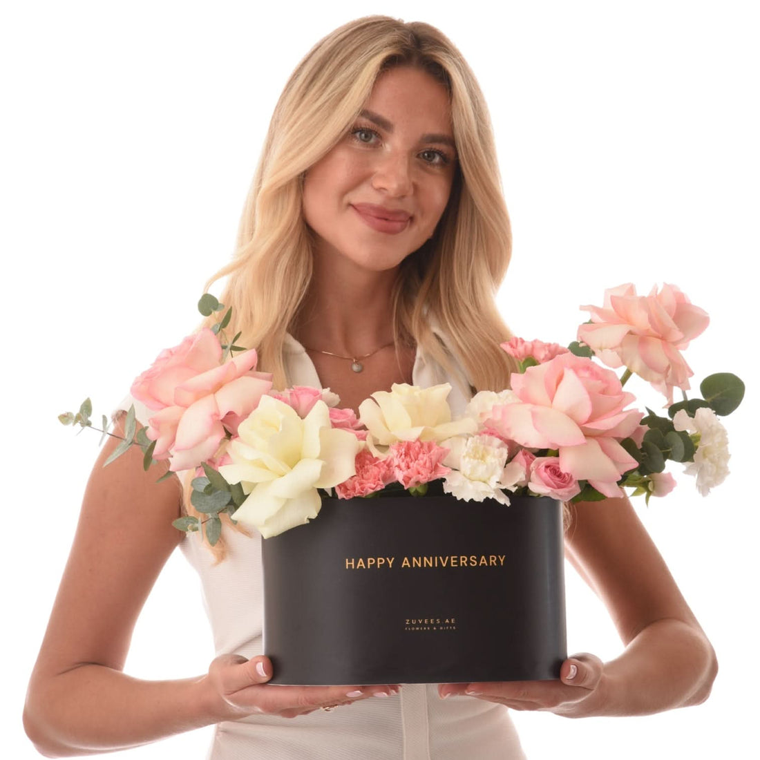 Blonde woman holds black "Happy Anniversary" floral box with pink, white roses and eucalyptus.