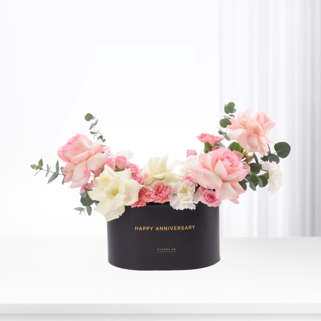 Elegant black box with "Happy Anniversary" in gold, overflowing with soft pink and white roses and eucalyptus.