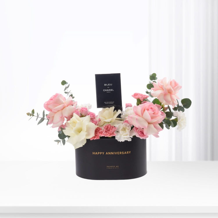 Black box with "Happy Anniversary" holds pink roses, carnations, and Chanel perfume.