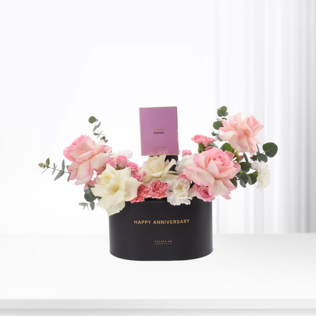 Elegant black anniversary box with pink roses, white blooms, and Chanel perfume.