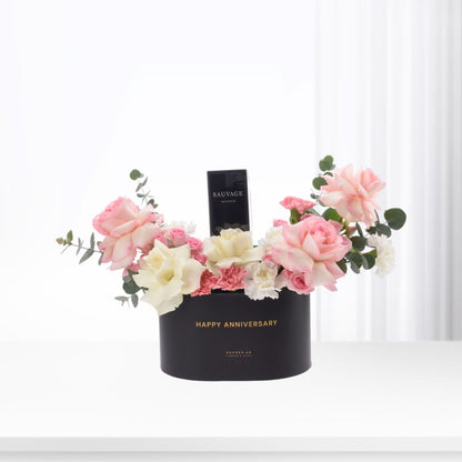 Black box with "Happy Anniversary" holds pink roses, white blooms, and Sauvage perfume.