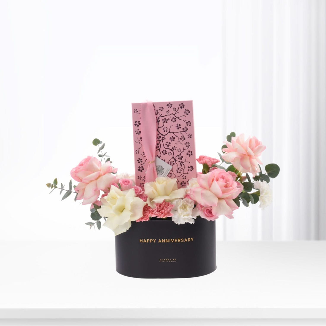 Elegant black box with "Happy Anniversary" holds soft pink, white roses and eucalyptus, accented by a pink cherry blossom gift tag.