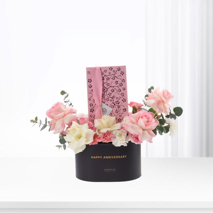 Elegant black box with "Happy Anniversary" holds soft pink, white roses and eucalyptus, accented by a pink cherry blossom gift tag.