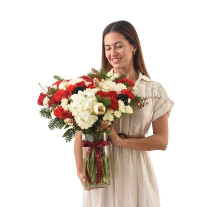 Woman smiles holding festive red-white floral arrangement with gold ornaments in glass vase.
