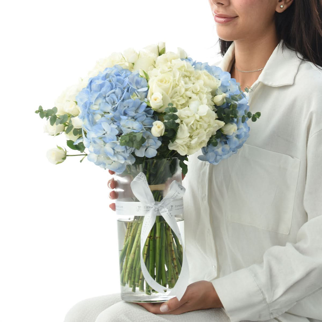Woman holding a vase of blue hydrangeas and ivory roses, flower delivery in Dubai