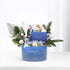 Blue holiday gift basket adorned with evergreens, cotton, pinecones, and festive cards.
