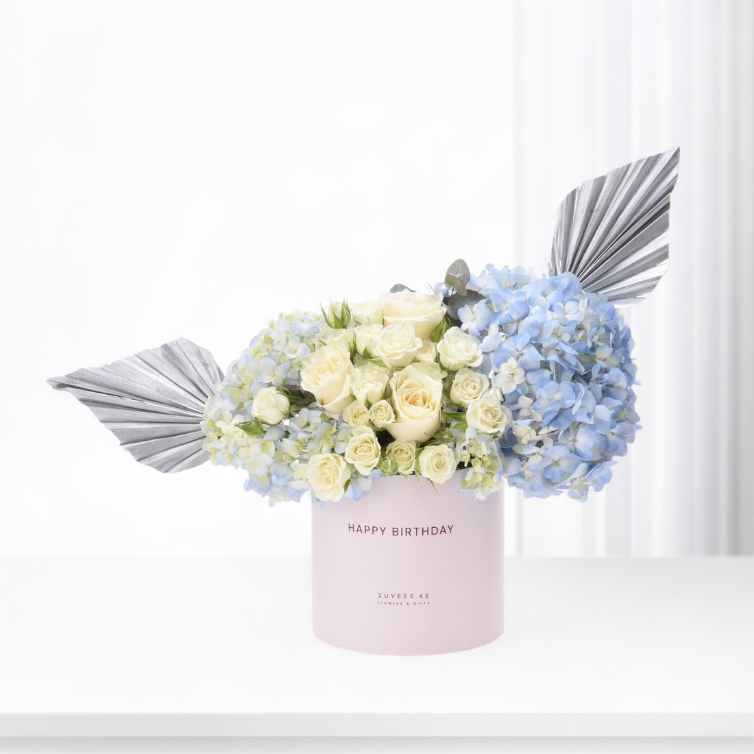 Elegant birthday bouquet in pastel pink box with silver leaf accents.