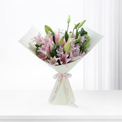 Soft pink lilies with green buds, elegantly wrapped in cream paper and pink ribbon.