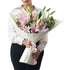 Elegant pink lilies in cream wrap, held by a woman in white blouse.