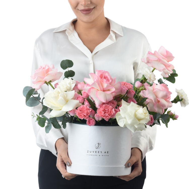 Elegant white hat box overflowing with soft pink and ivory roses, eucalyptus, and carnations.