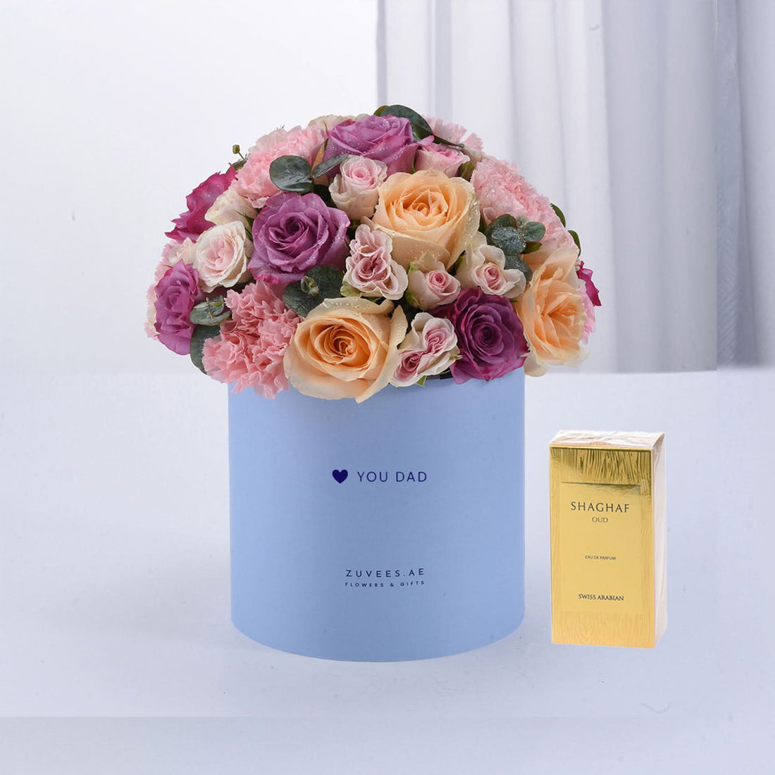Pastel roses and carnations in light blue box with "YOU DAD" message, beside gold Shaghaf Oud perfume.