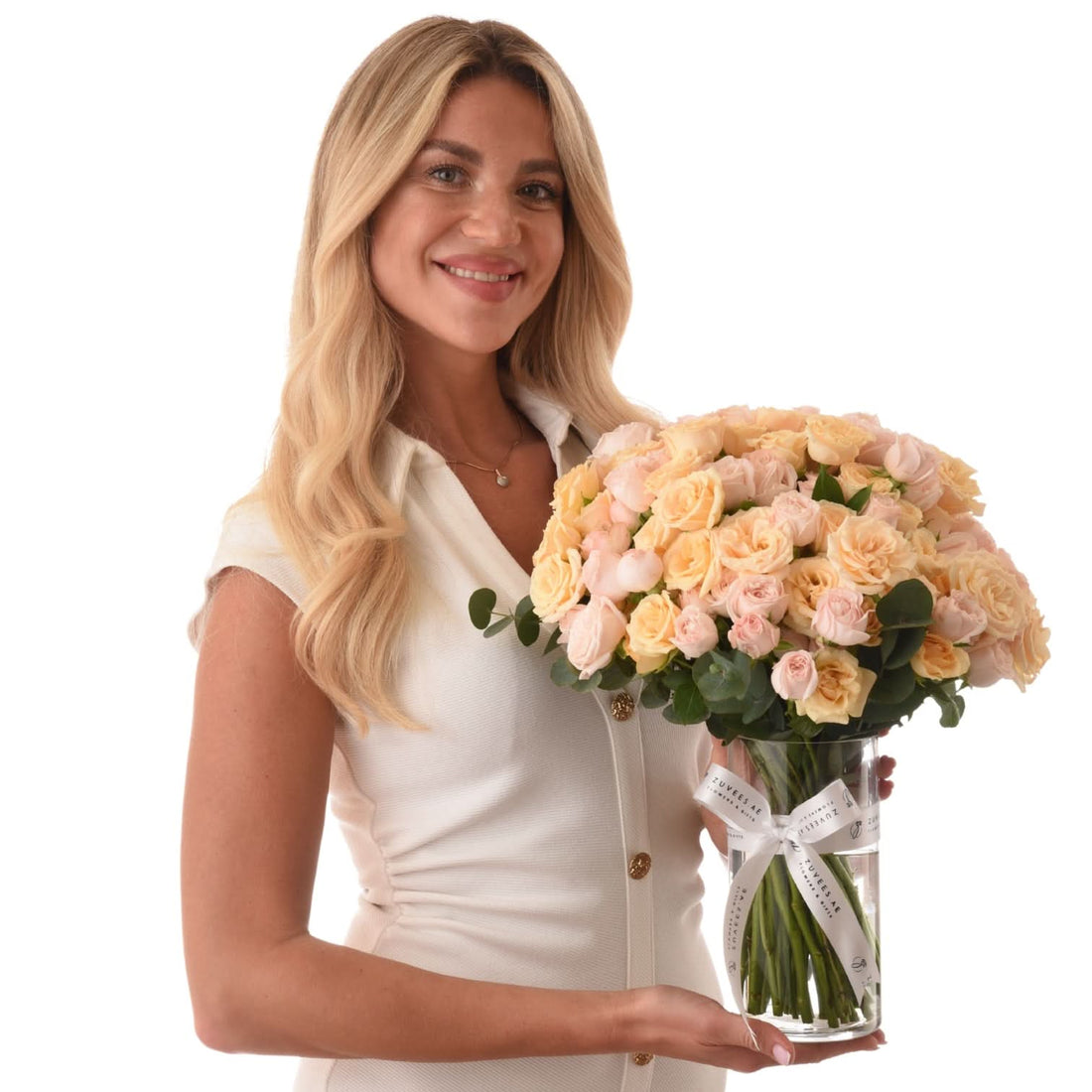 Woman holds lush peach rose bouquet in clear vase with branded ribbon.