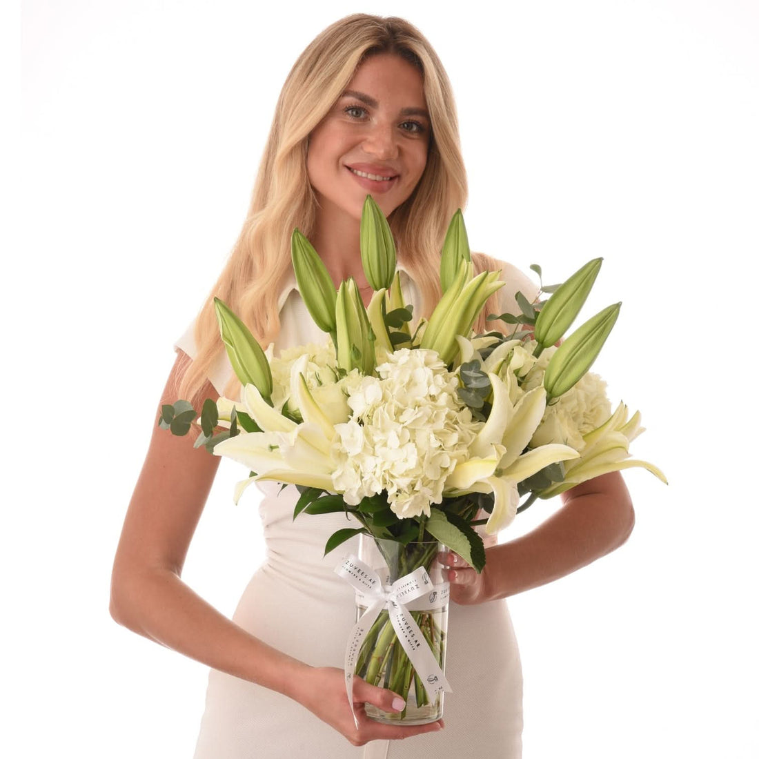 Woman holds elegant white lily and hydrangea bouquet in clear vase.