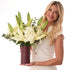 Elegant woman holds lush white lily and hydrangea bouquet in burgundy vase.