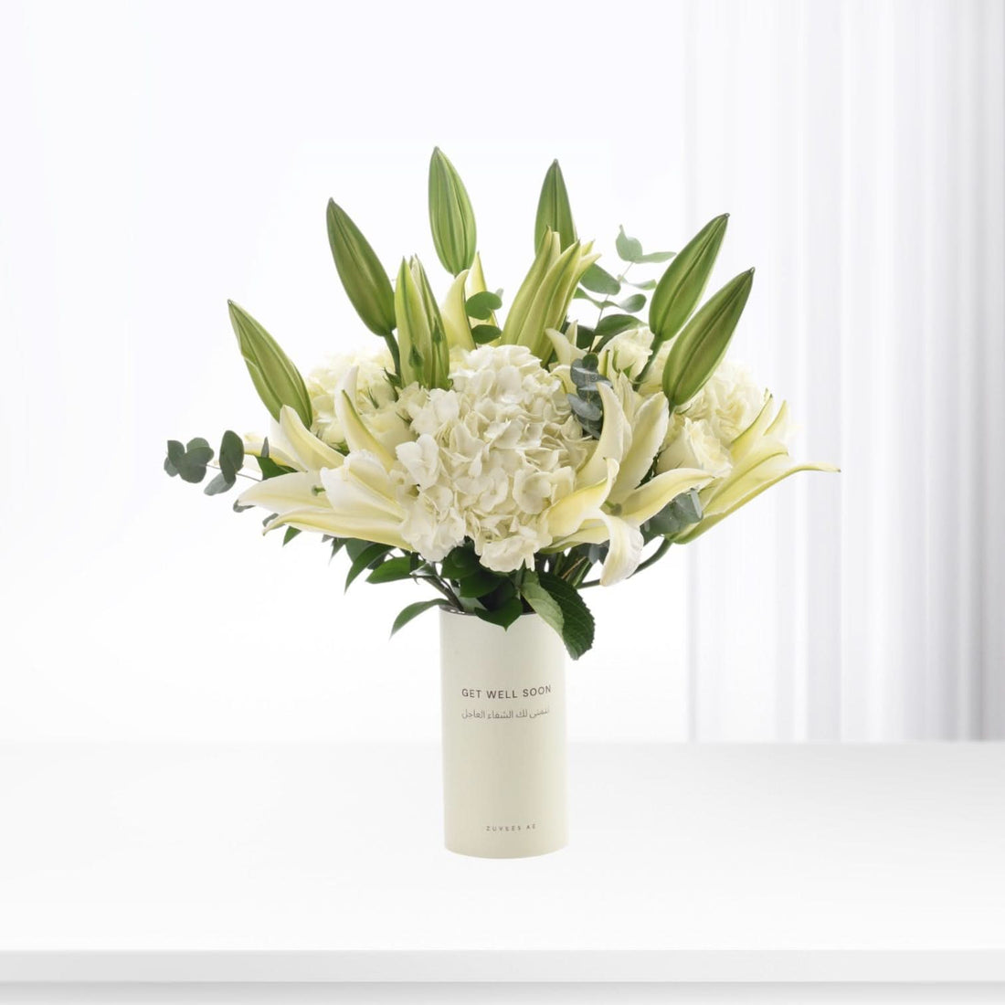 White lilies, hydrangeas, and buds in minimalist vase with "Get Well Soon" message.
