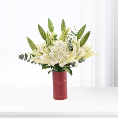 Elegant white lilies and hydrangeas in a bold red vase with heartfelt message.