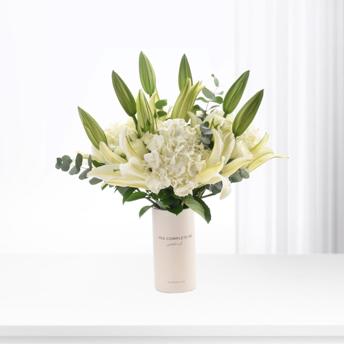 White lilies and hydrangeas in minimalist vase with bilingual message.