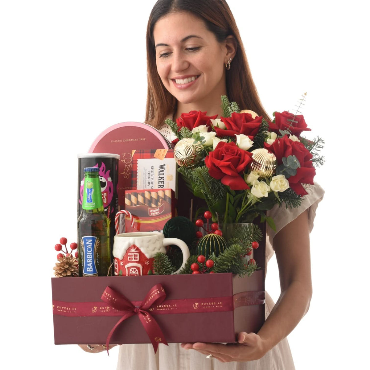 Woman holds festive gift basket with red roses, holiday treats, and Christmas decor.