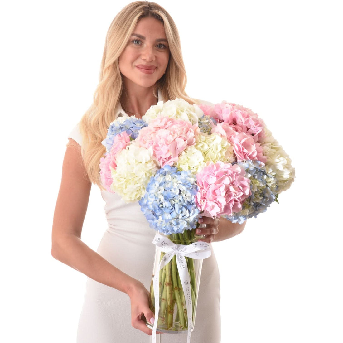 Woman holds pastel hydrangea bouquet in clear vase with white ribbon.