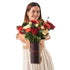 Woman holds festive red, white, and green floral arrangement in branded burgundy tube.