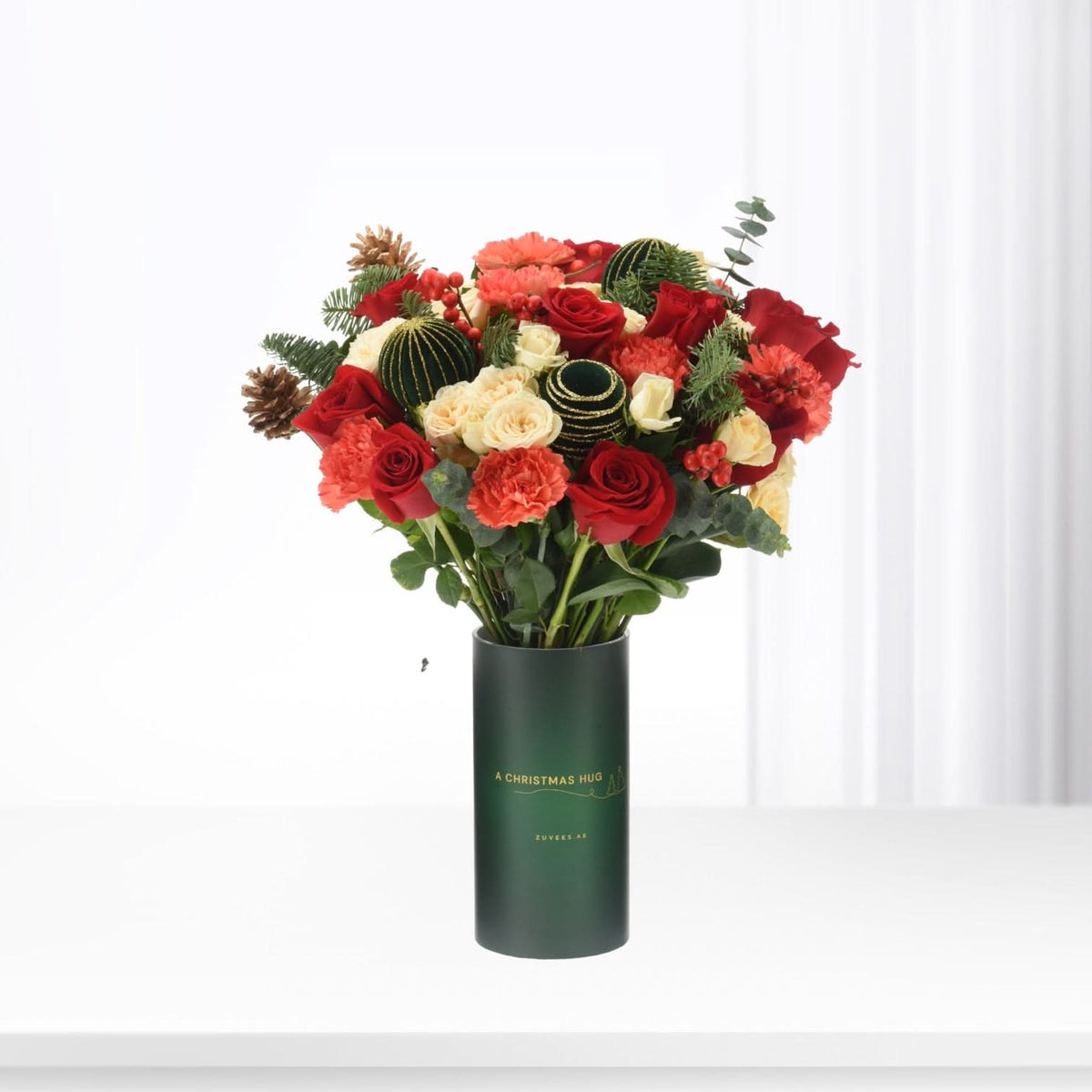 Vibrant red and cream roses, pinecones, and berries in festive green vase.